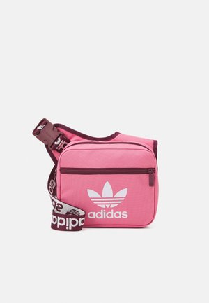 Sac à bandoulière Adidas rose avec poche zippée à l'avant, logo trèfle blanc, et sangle réglable arborant le branding Adidas en bordeaux et blanc.