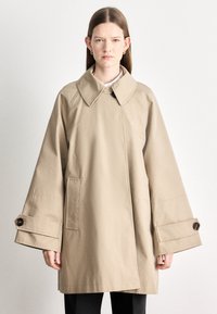 Bézs ballonkabát nagy gallérral, túlméretezett ujjakkal és mandzsettagombokkal. Elöl zsebekkel és egyenes szabású dizájnnal rendelkezik.