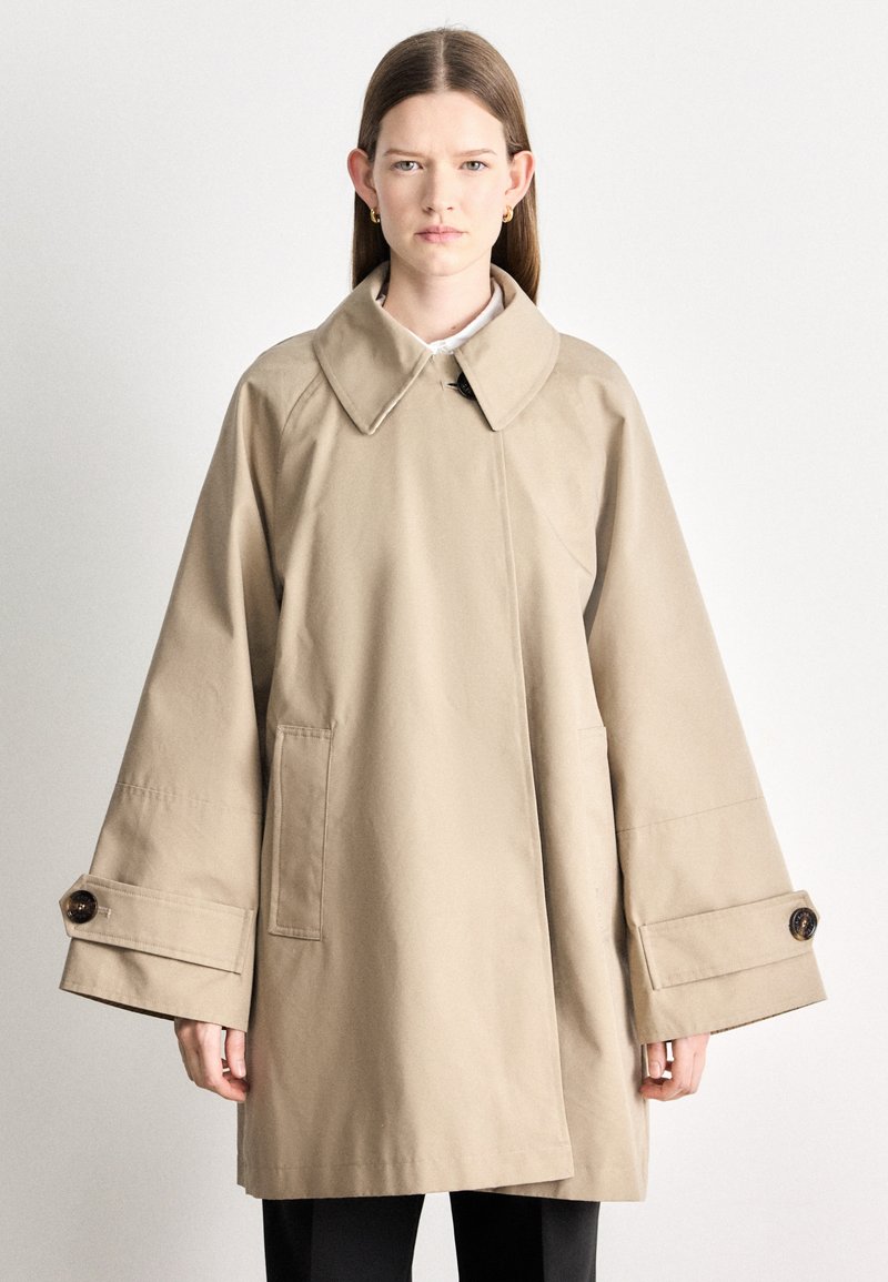 Bézs ballonkabát nagy gallérral, túlméretezett ujjakkal és mandzsettagombokkal. Elöl zsebekkel és egyenes szabású dizájnnal rendelkezik.