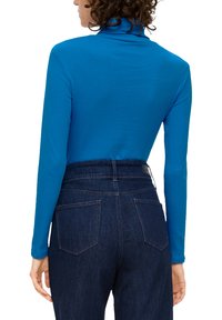 Langsleeve blauwe coltrui gecombineerd met high-waisted donkerdenim jeans met twee achterzakken en een subtiele stikselafwerking.