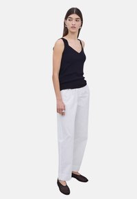 Top de tirantes negro con escote en V combinado con pantalones anchos blancos. La modelo lleva flats negros y pendientes de aro plateados. Acabados de tela suave.