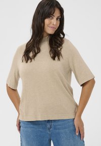 Beige kortærmet sweater med høj hals, lavet af blødt materiale. Letvægts og afslappet pasform, kombineret med blå denim jeans.