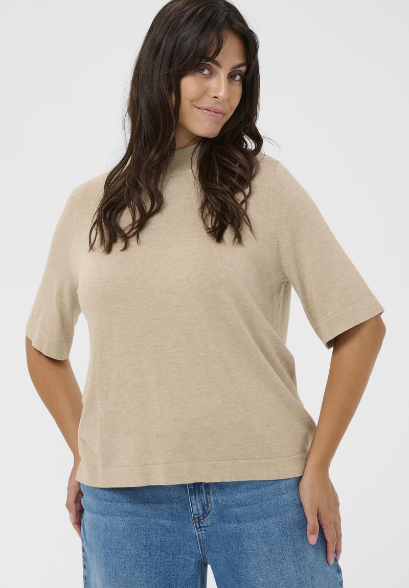 Beige kortærmet sweater med høj hals, lavet af blødt materiale. Letvægts og afslappet pasform, kombineret med blå denim jeans.