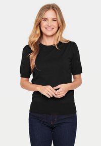 Black short-sleeve knit top with a crew neckline and ribbed hem. Displayed on a person wearing dark jeans, neutral background.