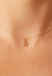 Gold pendant necklace featuring a capital letter "H," on a fine chain, with a smooth texture and a simple clasp.