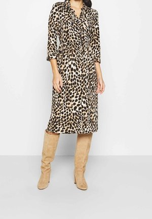 Kobieta ubrana w sukienkę w panterkę sięgającą kolan, z rękawami do połowy przedramienia, w połączeniu z wysokimi, zamszowymi, beżowymi kozakami do kolan.