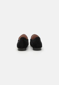 Mustat nubuk loaferit, joissa on sileä pinta, pyöristetyt takapuolet ja litteät pohjat. Ei näkyvää kiinnitystä tai koristeita. Yksinkertainen ja klassinen muotoilu.