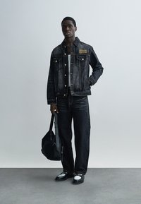 Σετ τζιν μπουφάν και τζιν παντελόνι σε σκούρο ίντιγκο, με χρυσές κεντητές λεπτομέρειες, κλασικές τσέπες και αντίθετη ραφή. Μαύρη τσάντα.