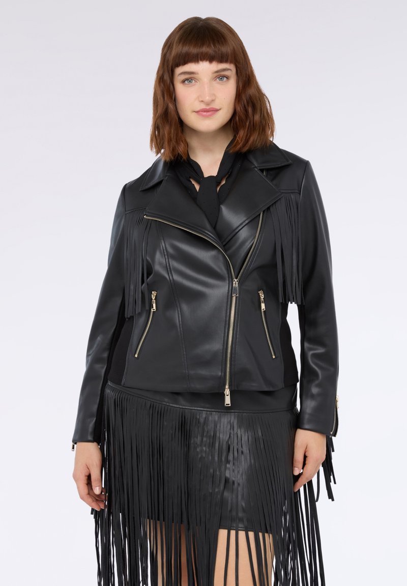 Giacca da biker in ecopelle nera con dettagli a frange, tasche con zip e design aderente, abbinata a una gonna coordinata.