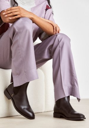Bottes de cheville en cuir marron avec un bout arrondi, des panneaux élastiques et un petit talon carré, associées à un pantalon large violet clair.