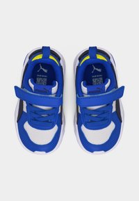 Παιδικά παπούτσια Puma σε μέγεθος για νήπια, λευκά και μπλε με κίτρινες λεπτομέρειες, διαθέτουν ιμάντες με βέλκρο και επάνω μέρος από διχτυωτό ύφασμα.