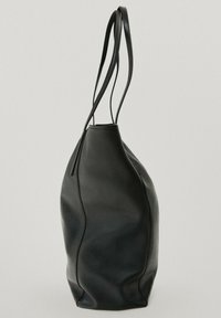 Musta nahkalaukku, jossa on sileä pinta, pyöreä muoto ja kaksi pitkää, hoikkaa kantohihnaa, jotka ulottuvat laukun ylimmästä osasta. Minimalistinen muotoilu.