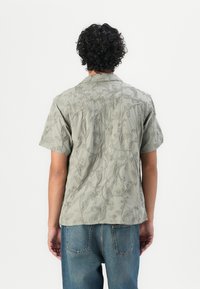 Kortermet skjorte i lysegrønn stoff med brodert blomsterdesign. Har klassisk krage og avslappet passform. Brukt med denimjeans.