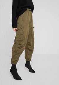 Olijfgroene cargobroek met trekkoord in de taille, elastische boorden en zijzakken, gecombineerd met zwarte geribbelde enkelboots en een zwarte trui.