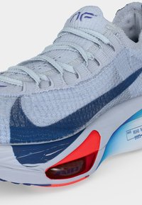 Ανοιχτό μπλε αθλητικό παπούτσι Nike με σκούρο μπλε swoosh, λευκά κορδόνια και ορατό κόκκινο αερόσακο στην σόλα.