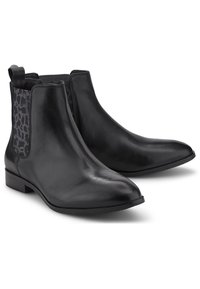Botas de piel negras hasta el tobillo con punta afilada, paneles laterales texturizados en negro y un tacón bajo tipo bloque. Cuenta con una asa en la parte trasera para facilitar su colocación.