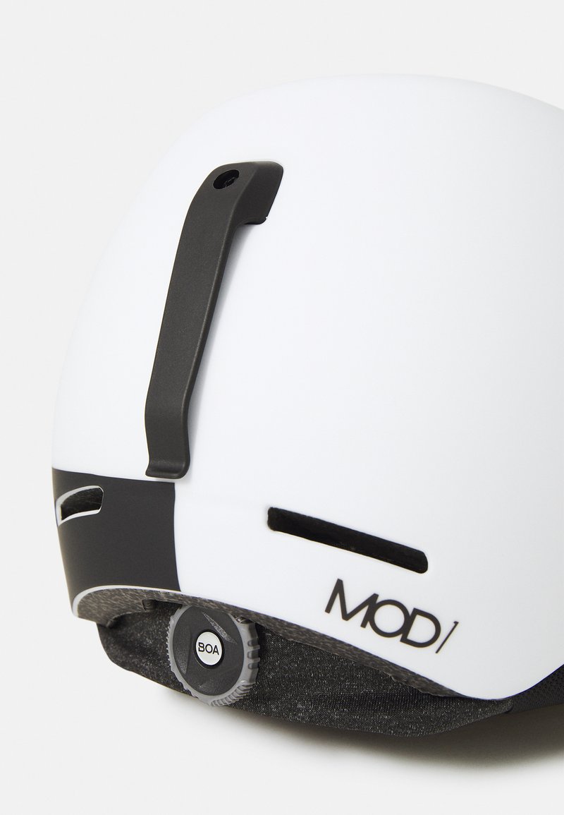 Weißer Helm mit matter Oberfläche. Ausgestattet mit einem schwarzen Einstellrad, seitlichen Belüftungsöffnungen und einem Clip zur Befestigung. Das Branding "MOD/" ist sichtbar.
