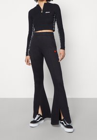 Svart cropped zip-up topp med långa ärmar, och svarta utsvängda sweatpants med sidoklyftor och en liten logotyp. Svarta sneakers.