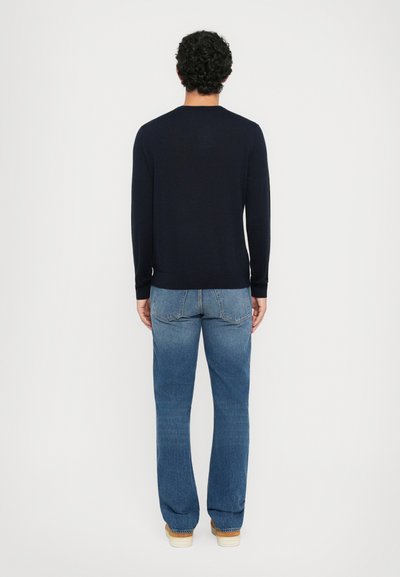 Marineblauer Langarmpullover mit Rundhalsausschnitt, kombiniert mit hellblauen, geraden Jeans und braunen Schuhen; sichtbare gerippte Bündchen und Saum.
