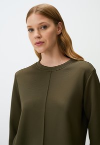 Felpa verde oliva, con texture, a girocollo e cuciture sottili. Tessuto morbido con silhouette aderente.