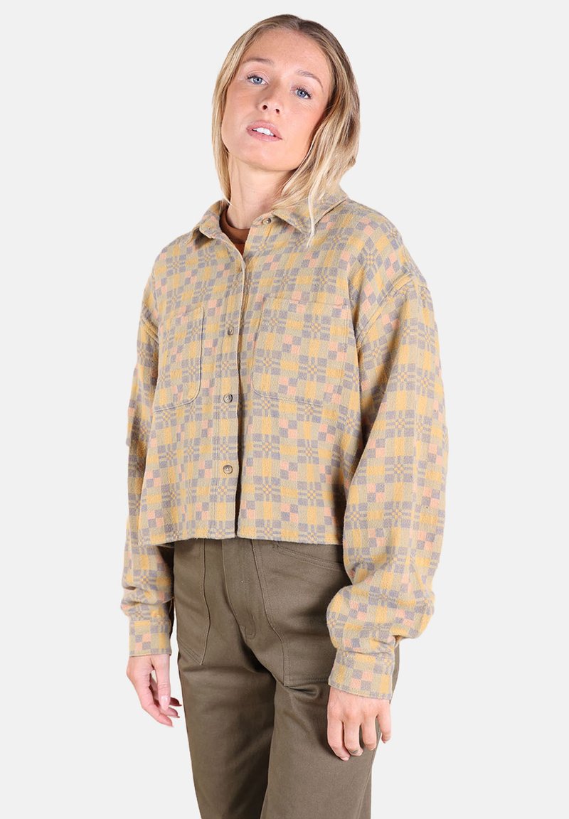 Chemise en flanelle courte aux motifs à carreaux jaunes, gris et lilas, avec un col, une fermeture à boutons et des manches longues.