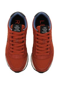 Ein Paar rote Laufschuhe mit Schnürung, blauer Innenausstattung und schwarzem Zungenetikett mit der Aufschrift "LÄUFE SCHNELLER ALS DU KANNST."