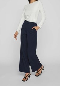 Breda marinblå byxor med skräddarsydd passform, med sidofickor. Kombineras med en långärmad vit topp och svarta klacksandaler.