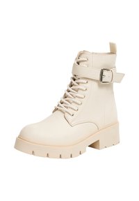 Stivaletti beige con lacci, dotati di una cinghia con fibbia, texture liscia, suola grossa e punta tonda. Presentano un pratico gancio sul tallone.