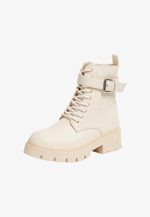 Stivaletti beige con lacci, dotati di una cinghia con fibbia, texture liscia, suola grossa e punta tonda. Presentano un pratico gancio sul tallone.