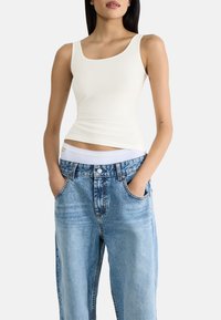 Vit åtsittande linne med rundad halsringning, kombinerat med ljusblå högmidjade jeans. Jeansen har en avslappnad passform och traditionella fickor.