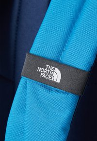 Tira de tecido azul com uma superfície texturizada, apresentando um rótulo preto impresso com "THE NORTH FACE" e um detalhe em branco do logotipo.