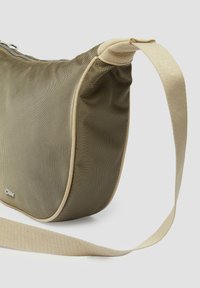 Gestructureerde olijfgroene tas met een zachte beige rand, voorzien van een schouderband en een ritssluiting langs de bovenrand.