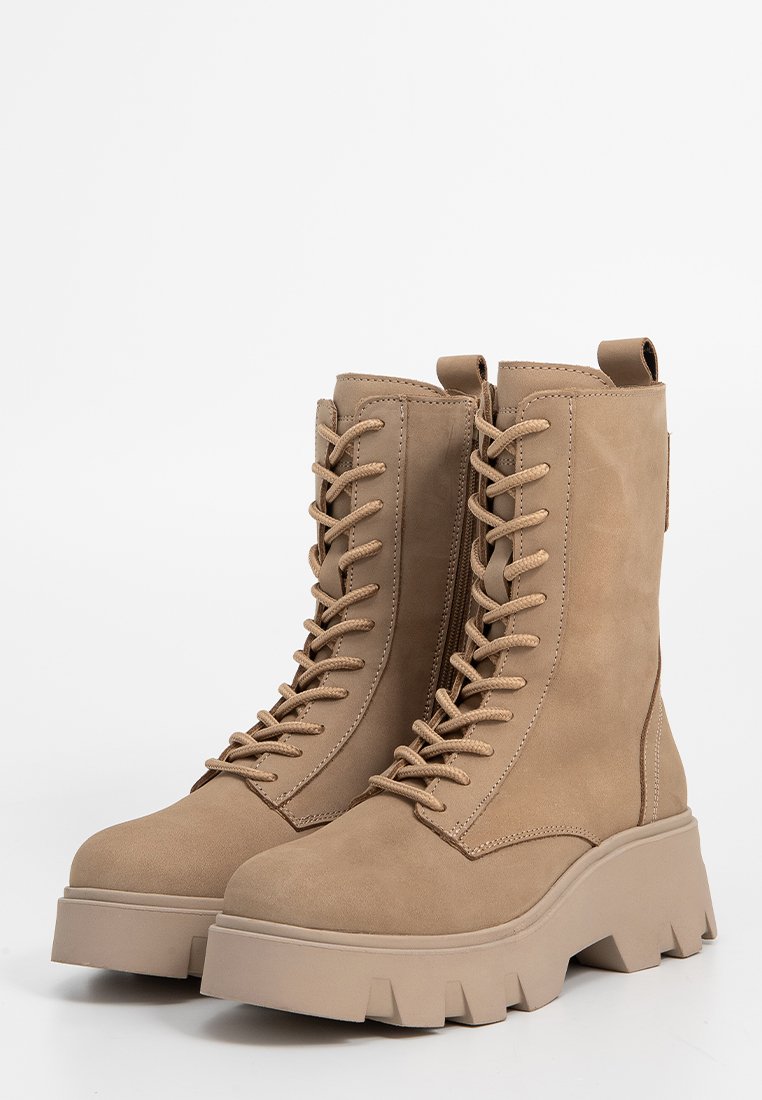 Ein Paar beiger Schnürkampfboots mit klobigen, gerillten Sohlen und seitlichen Reißverschlüssen vor einem schlichten weißen Hintergrund.