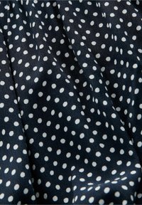 Merikankaan kangas, jossa on valkoisia vaihtelevan kokoisia pilkkuja, sileä ja hennosti kiiltävä pinta.