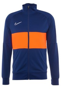 Veste zippée bleu marine avec une section horizontale orange vif sur la poitrine. Comporte le logo Nike en blanc et des poignets côtelés.