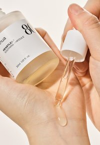 Bottiglia di vetro trasparente etichettata "80 Heartleaf Soothing Ampoule", riempita con un liquido chiaro. Pipetta che rilascia una goccia sul palmo.