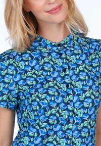 Floral short-sleeve shirt featuring a navy blue background with blue and green floral patterns, rounded collar, and button closure.