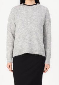 Vaaleanharmaa neulottu neulepaita pyöreällä pääntiellä, ribbineuloksisilla hihojen resoreilla ja hieman väljä istuvuus. Pehmeä pinta ja näkyvät ompelusaumat helmassa.