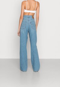 Jeans en denim bleu clair taille haute avec des jambes larges, dotés de poches arrière et d'un patch en cuir à la taille. Texture douce.