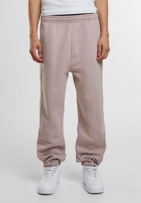 Pantaloni de trening roz deschis, cu talie elastică, buzunare și manșete conice. Asortați cu adidași albi, având o textură netedă.