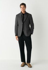 Blazer grigio in lana con rever a contrasto, chiusura a singolo bottone e due tasche frontali; abbinato a pantaloni neri e mocassini marroni.