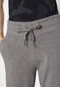 Calças de fato cinzas com uma textura suave, apresentando um cós ajustável e bolsos. O tecido é liso e casual, adequado para o lazer.