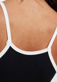 Top nero a coste con bordo bianco che mostra spalline sottili e una vista ravvicinata del tessuto testurizzato sulla pelle.