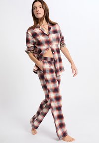 Conjunto de pijama a cuadros en rojo, azul marino y crema. Material de franela, camisa de botones con detalles de abertura lateral, bolsillos y pantalones con cinturilla elástica.