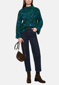 Green sweater with blue leaf pattern, dark blue denim pants, brown suede ankle boots, and a brown crossbody bag with a flap closure.