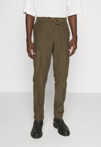 Olivgröna byxor i texturerat tyg, med dragsko i midjan, avsmalnande ben och sidofickor. Bärs tillsammans med svarta stövlar.