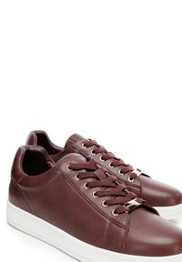 Sneakers in pelle bordeaux con una texture liscia, occhielli dorati e suole in gomma bianca. Design con lacci e punta rotonda.