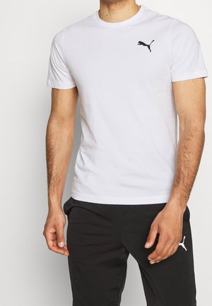 Homme portant un t-shirt blanc Puma avec un logo noir sur la poitrine et un pantalon noir Puma avec un logo blanc sur la cuisse.
