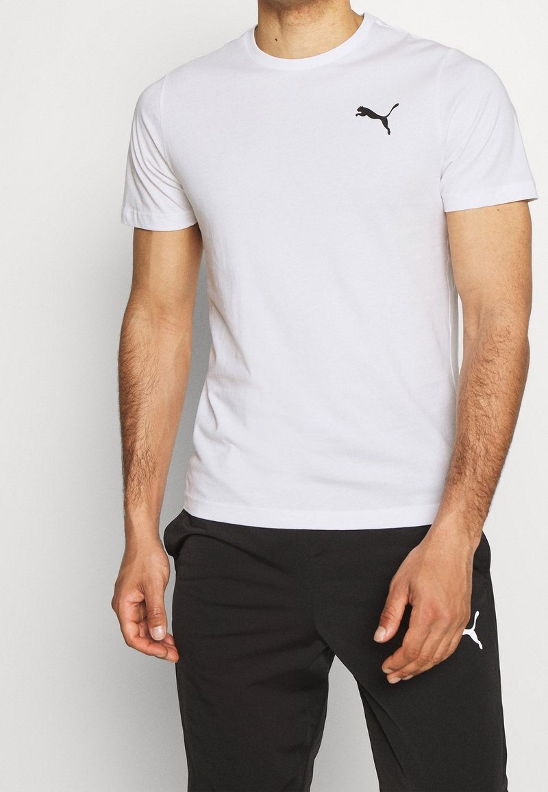 Homme portant un t-shirt blanc Puma avec un logo noir sur la poitrine et un pantalon noir Puma avec un logo blanc sur la cuisse.