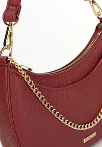 Rote, strukturierte Lederhandtasche mit geschwungener Form. Mit goldener Kettenverzierung, Reißverschluss und Markenlogo-Plakette.